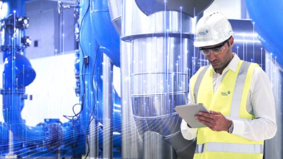 A person wearing a safety vest and hardhat looking at a tablet