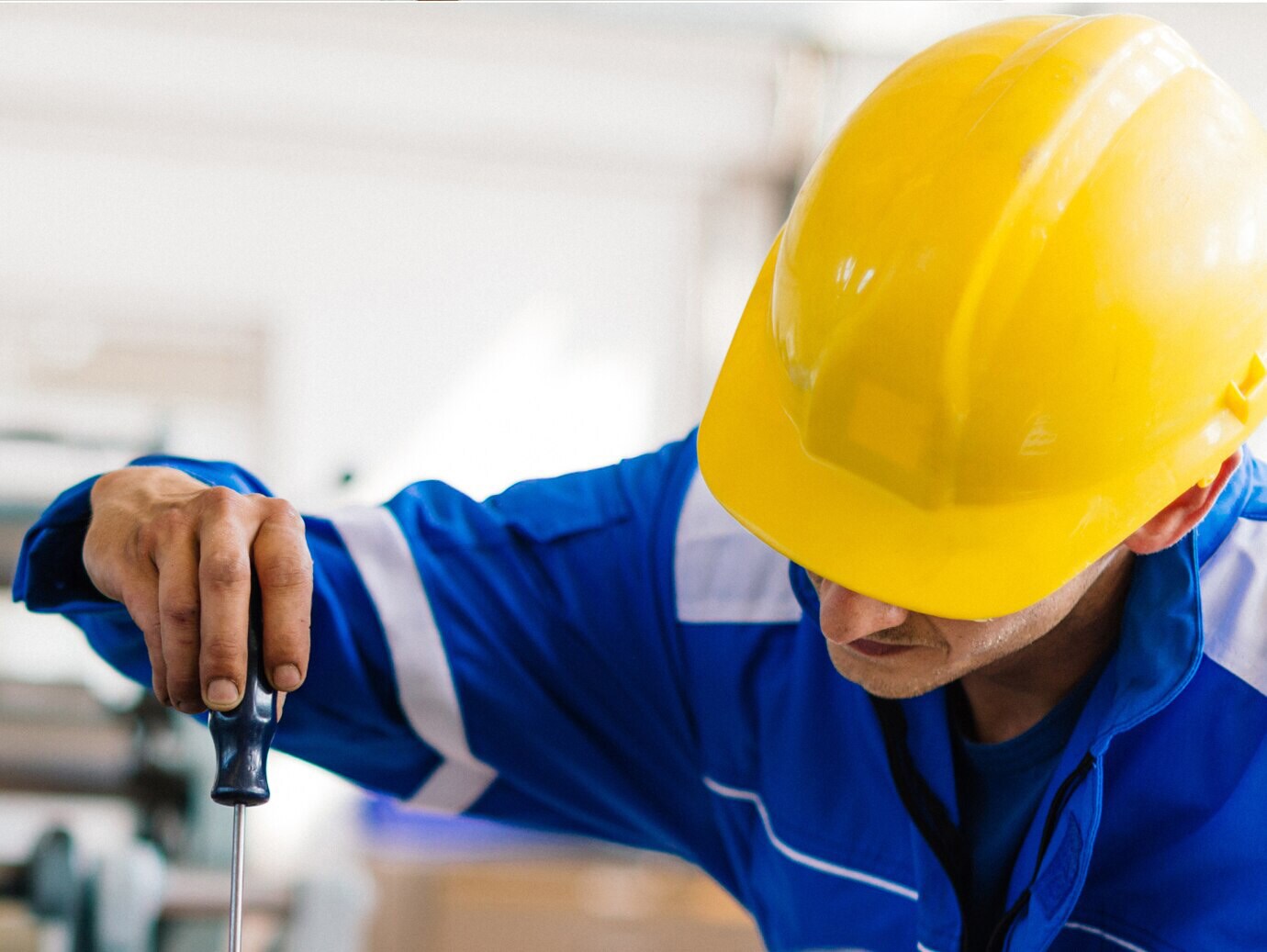 An engineer in protective gear turning a screwdriver on an object 