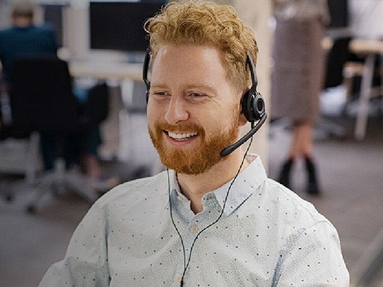 Customer support agent wearing headphones smiling while working on his desktop