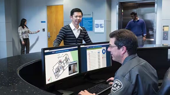 Security officer working on a computer at the front desk, as a customer watches