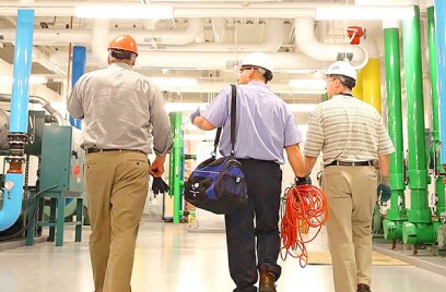 Back view of three men walking inside an industrial facility